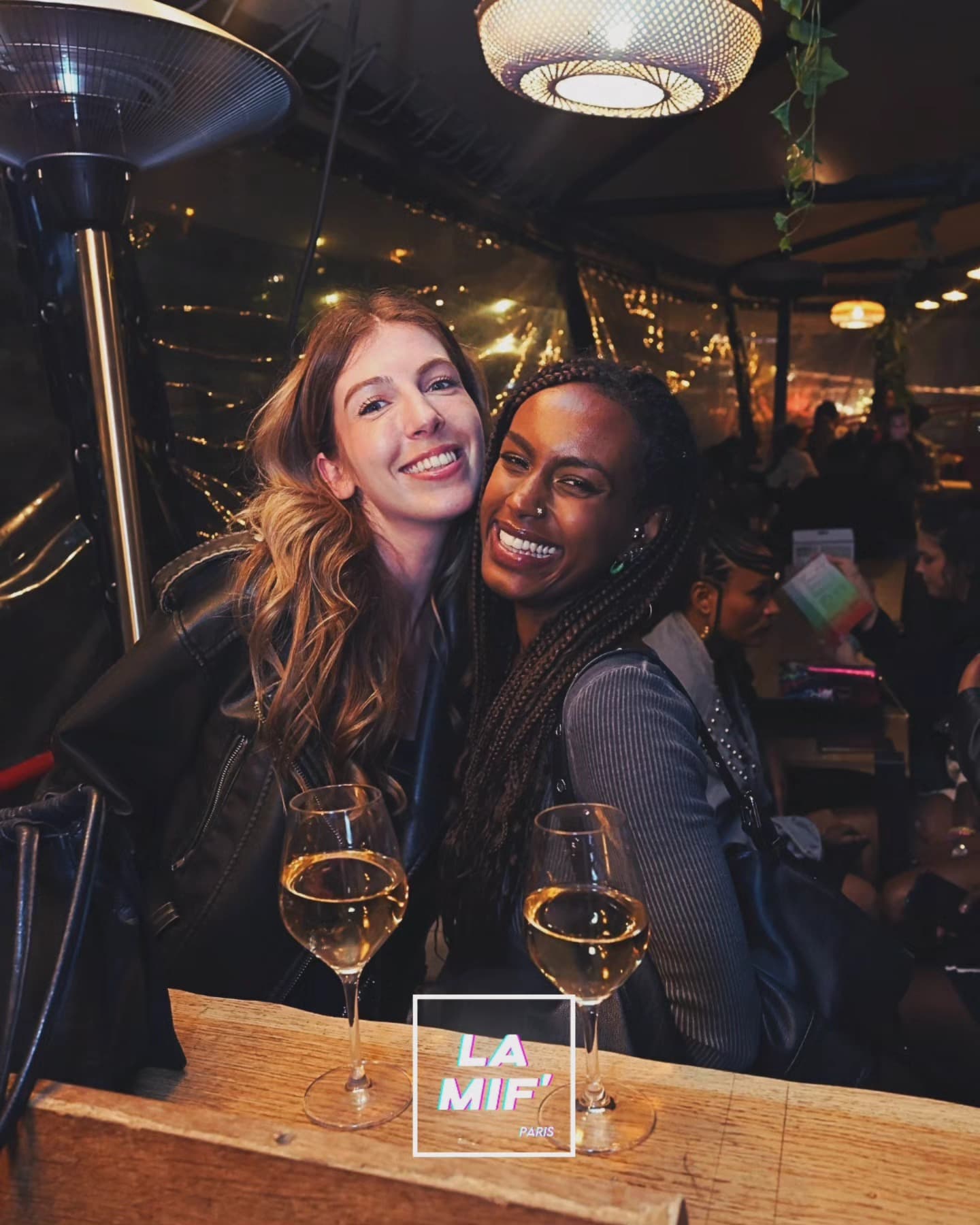 Deux amies enlacées et rieuses, verres de vin blanc à la main